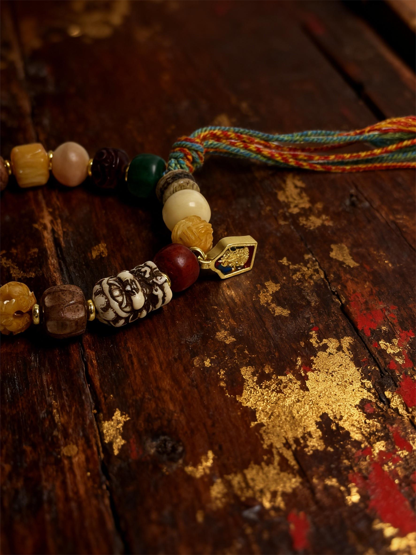 Close-up detail of the Pangu inspired After the Divide bracelet (12mm) featuring mixed beads, a colorful tassel cord and gold charm on a vintage wood background with golden texture accents