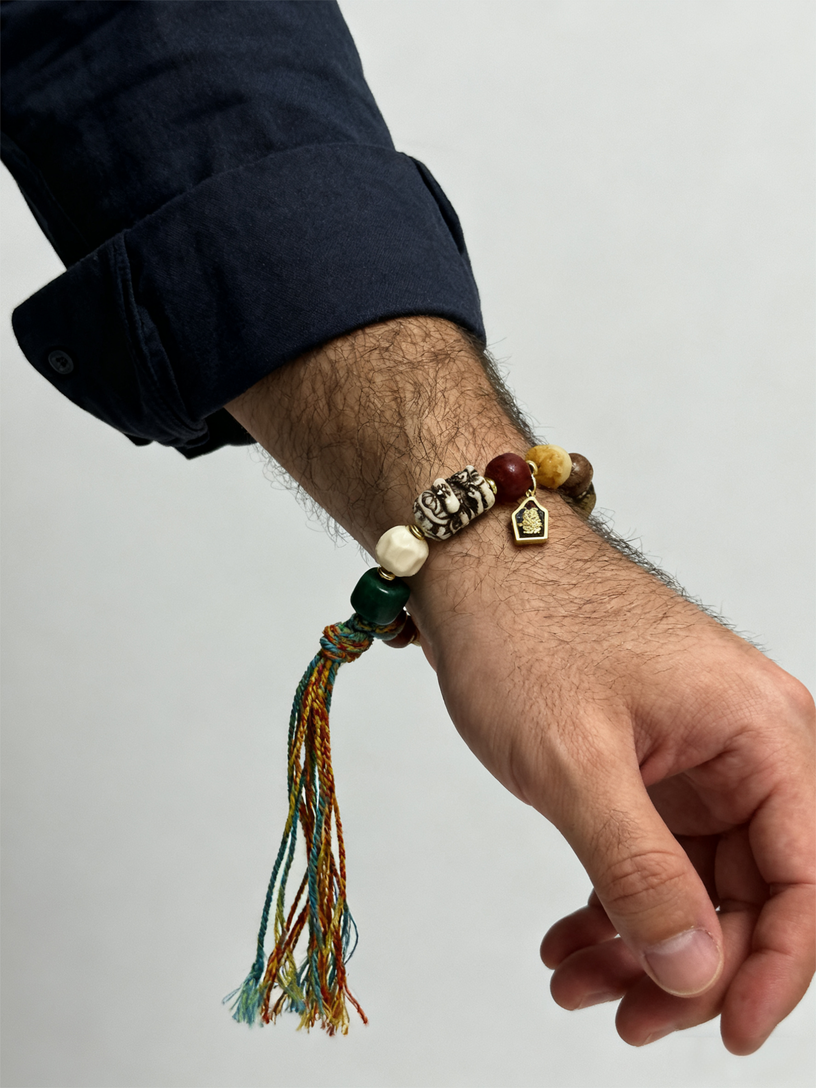 Side close-up of a man wearing the Pangu inspired After the Divide bracelet (12mm) showing the colorful tassel cord, gold charm and mixed beads