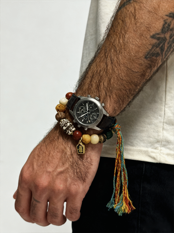Man styling the Pangu inspired After the Divide bracelet (12mm) with a watch, featuring mixed material beads, a colorful tassel cord and gold charm details