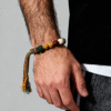 Man wearing the Pangu inspired After the Divide bracelet (12mm) featuring mixed material beads, a colorful tassel cord and gold charm on a clean background