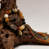 Pangu inspired After the Divide bracelet (12mm) with mixed material beads, colorful tassel cord and gold charm styled on a natural wood root background