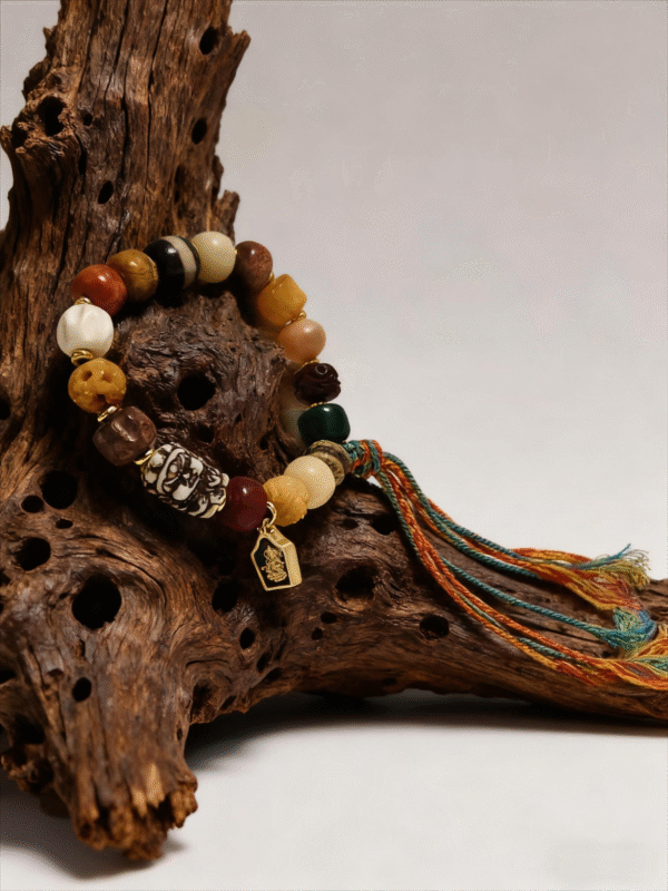 Pangu inspired After the Divide bracelet (12mm) with mixed material beads, colorful tassel cord and gold charm styled on a natural wood root background