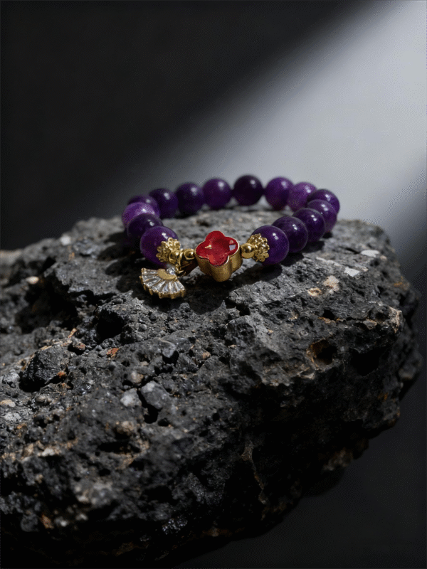 Close-up of the Nüwa inspired Blessed Heart amethyst bracelet (11mm) featuring purple beads, gold accents and a red heart charm on a rock background