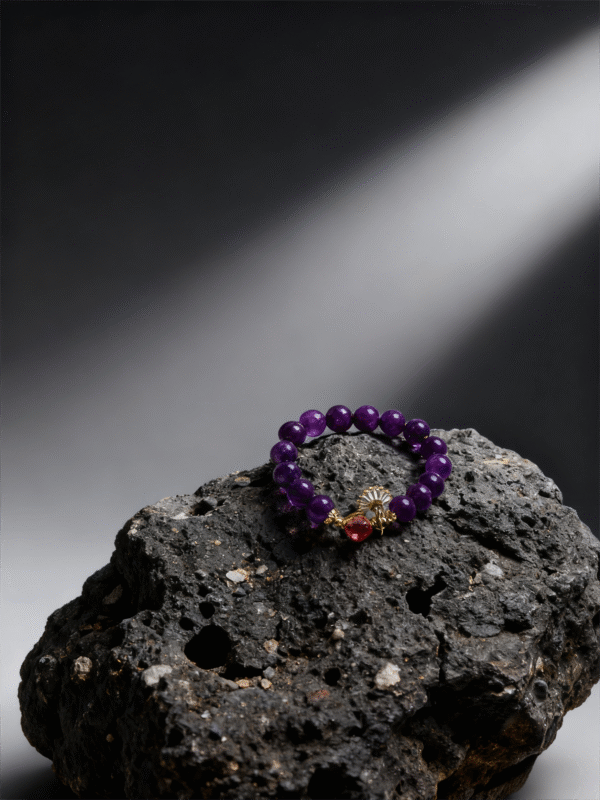 Nüwa inspired Blessed Heart amethyst bracelet (11mm) styled on a textured rock background with purple beads, gold details and a red heart charm