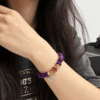 Woman wearing the Nüwa inspired Blessed Heart amethyst bracelet (11mm) with purple beads, gold accents and a red heart charm in a casual close-up wrist shot