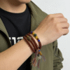 Bound Resolve Red Agate Bracelet 10mm – Xingtian Inspired Men’s Styling Shot with Watch Men wearing the Xingtian inspired Bound Resolve red agate bracelet (10mm) in a multi-wrap style with colorful accent beads and tassel charms on a clean white background