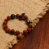 Bound Resolve Red Agate Bracelet 10mm – Xingtian Inspired Product Shot on Wooden Table Product shot of the Xingtian inspired Bound Resolve red agate bracelet (10mm) with faceted red beads, patterned accent beads and gold details on a burlap and wooden table background