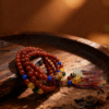 Bound Resolve Red Agate Bracelet 10mm – Xingtian Inspired Product Styling Shot in Warm Light Xingtian inspired Bound Resolve red agate bracelet (10mm) styled on a warm wooden surface with colorful accent beads and tassel charms in a cozy atmosphere