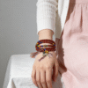 Bound Resolve Red Agate Bracelet 10mm – Xingtian Inspired Women’s Wearing Shot (Multi-Wrap Styling) Woman wearing the Xingtian inspired Bound Resolve red agate bracelet (10mm) in a multi-wrap style with colorful accent beads and tassel charms, styled for a soft everyday look