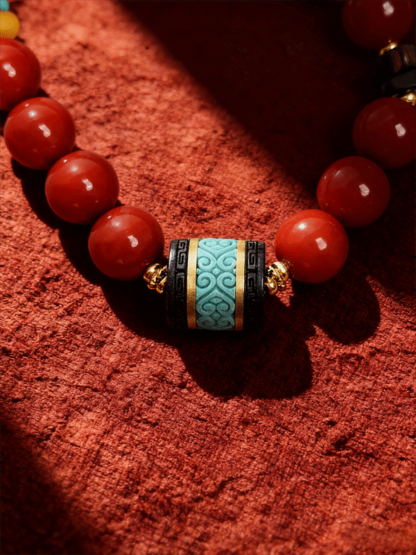 Close-up of the Bound Resolve Red Agate Bracelet featuring red agate beads and a turquoise-toned centerpiece on a textured red background.