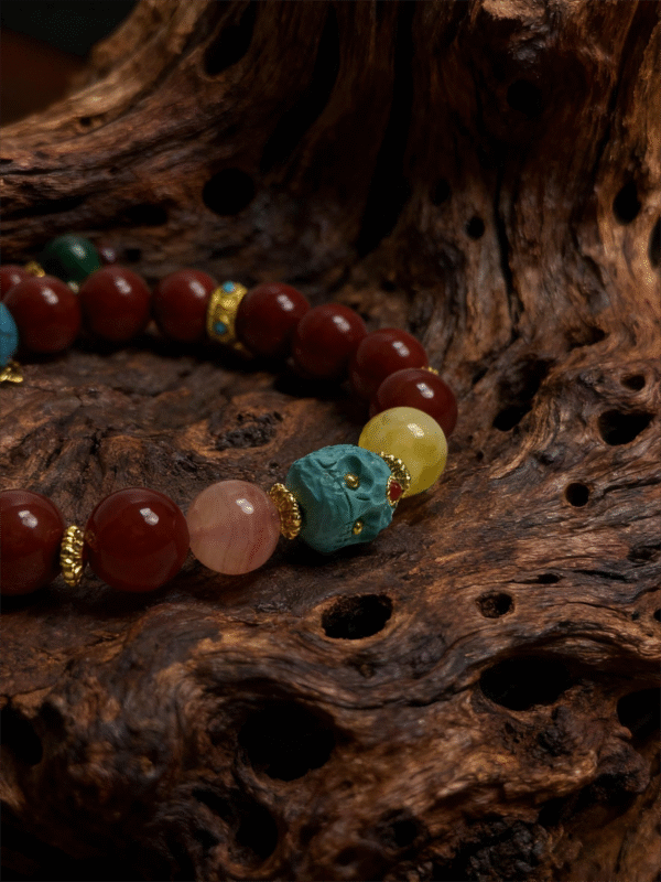 Crimson Fury & Turquoise Totem Bracelet from the Xingtian Myth Collection, featuring polished red cinnabar beads, deep green jade stones, a carved turquoise totem centerpiece, and gold-tone spacer accents. The 10mm beaded bracelet is displayed on a textured natural wood background, highlighting its bold mythological design, handcrafted details, and rich contrast of red, green, and turquoise tones.