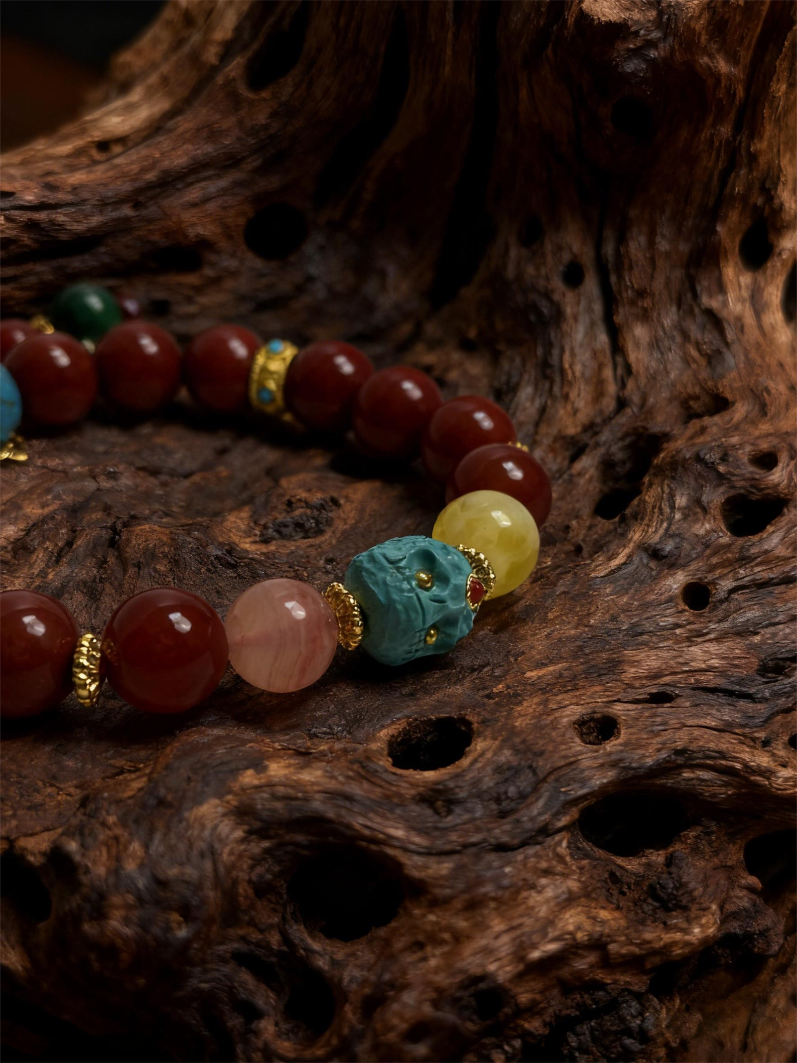Crimson Fury & Turquoise Totem Bracelet from the Xingtian Myth Collection, featuring polished red cinnabar beads, deep green jade stones, a carved turquoise totem centerpiece, and gold-tone spacer accents. The 10mm beaded bracelet is displayed on a textured natural wood background, highlighting its bold mythological design, handcrafted details, and rich contrast of red, green, and turquoise tones.