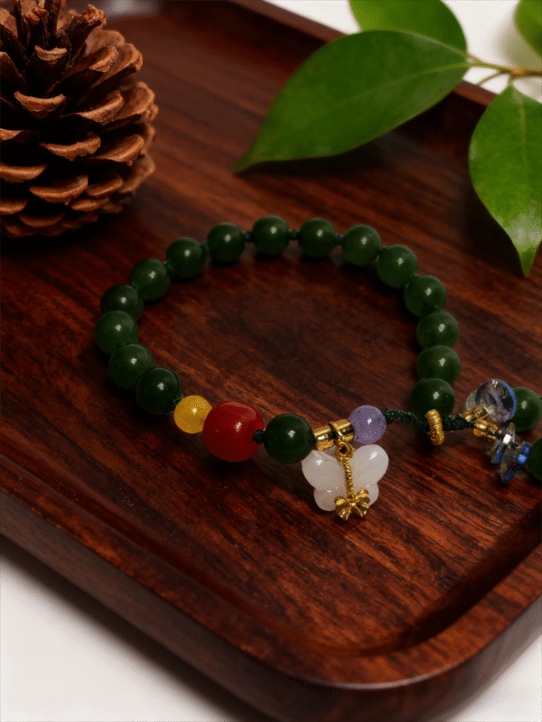 Crimson Herbfruit Jade Bracelet – Shennong Edition (10mm), handcrafted green jade bead bracelet with red and yellow accent stones, natural crystal charm and gold-tone details, displayed on a dark wooden tray with pine cones and green leaves, inspired by Shennong and traditional Chinese herbal symbolism