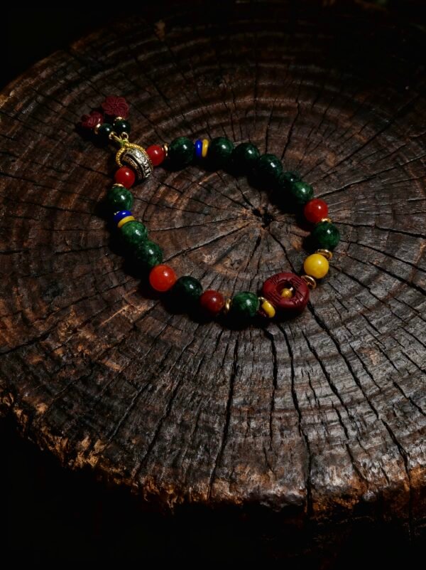 Handcrafted Crimson Seal & Jade Grove Bracelet inspired by Shennong, featuring deep green jade beads, vivid cinnabar-red focal bead engraved with ancient symbols, gold-tone spacers, and traditional color accents, displayed on a natural aged wood surface that highlights the bracelet’s earthy textures, mythological symbolism, and refined artisan craftsmanship.