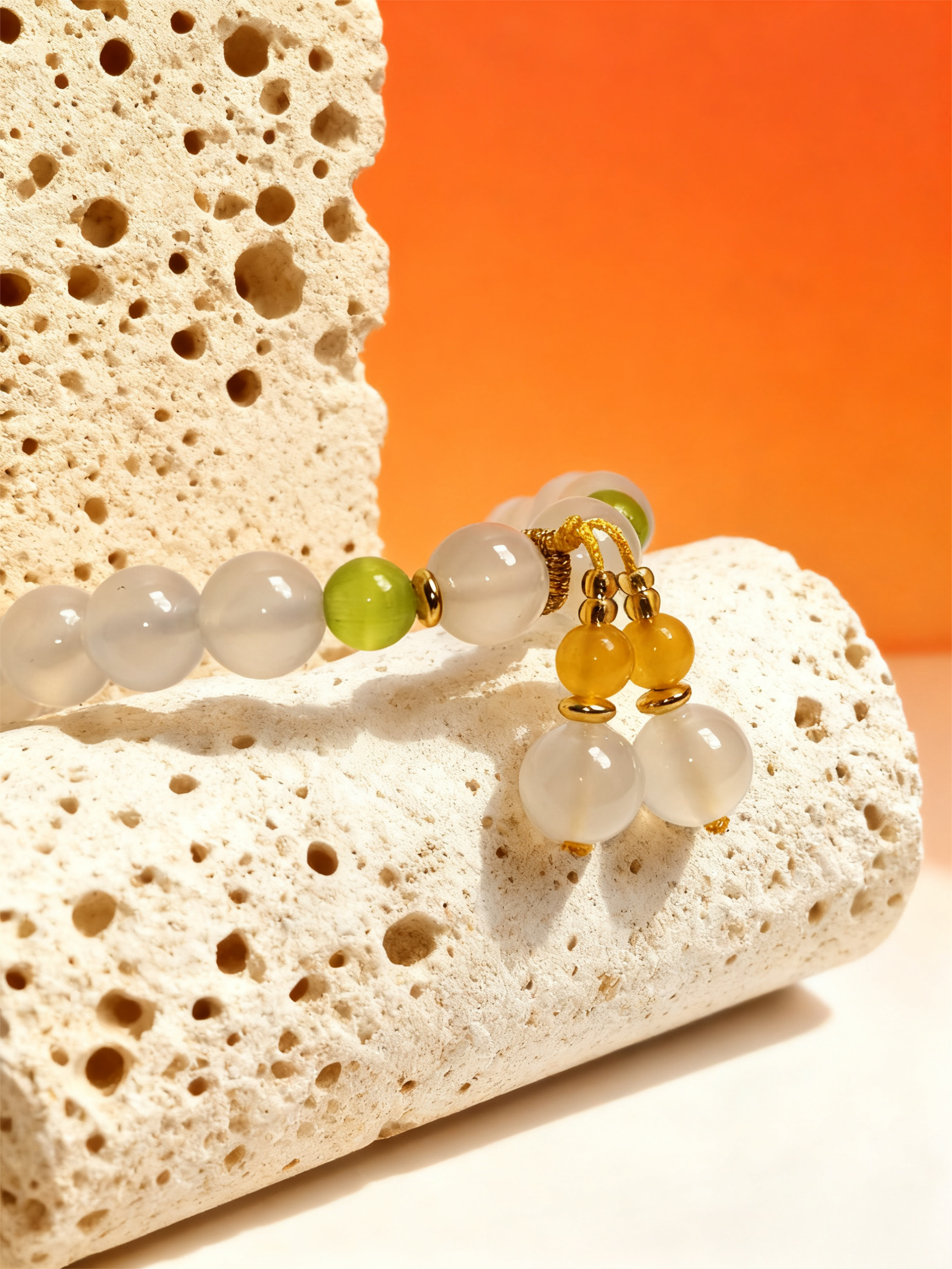 Detailed close-up of the Chang’e inspired Goddess Moonstone & Sunrise Agate bracelet highlighting polished moonstone beads, translucent green and golden agate accents, and refined gold metal elements, resting on textured stone under warm orange lighting to emphasize craftsmanship, balance, and mythological elegance.
