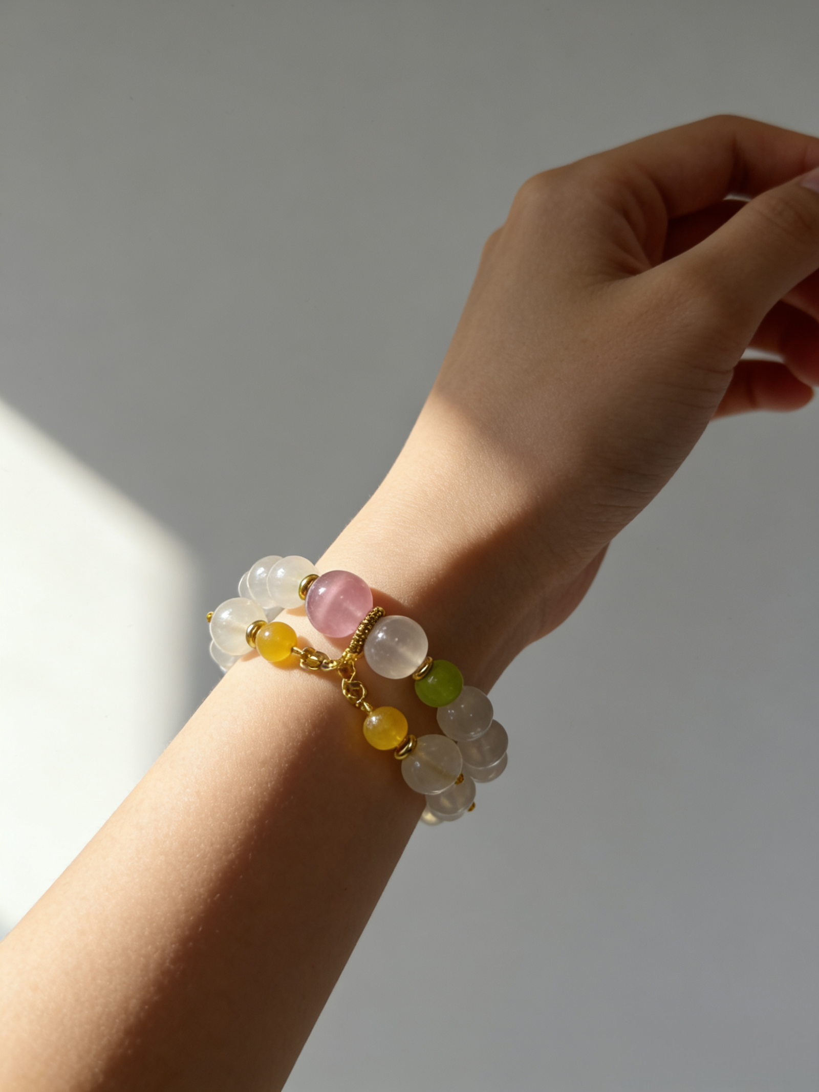 Lifestyle wrist shot of the Chang’e inspired Goddess Moonstone & Sunrise Agate bracelet, featuring luminous 10mm moonstone beads, a soft pink sunrise agate centerpiece, green and golden accent stones, and refined gold details, worn on the wrist in gentle natural light against a minimal background, expressing lunar grace, feminine warmth, and serene celestial elegance.