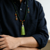 Close-up of a man styling the Shennong inspired Herbal Way bracelet (8mm) as a necklace with green beads, colorful accents and a green tassel pendant over a dark shirt