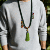 Man wearing the Shennong inspired Herbal Way bracelet (8mm) as a necklace, featuring dark green beads, colorful accents and a green tassel pendant in outdoor light