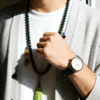 Man styling the Shennong inspired Herbal Way bracelet (8mm) as a necklace with a watch, featuring green beads, colorful accent beads and a tassel pendant in natural window light