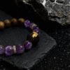 Close-up of the Nüwa inspired Mother of Earth bracelet (11mm) featuring purple beads, a wood accent bead and gold details on a stone background