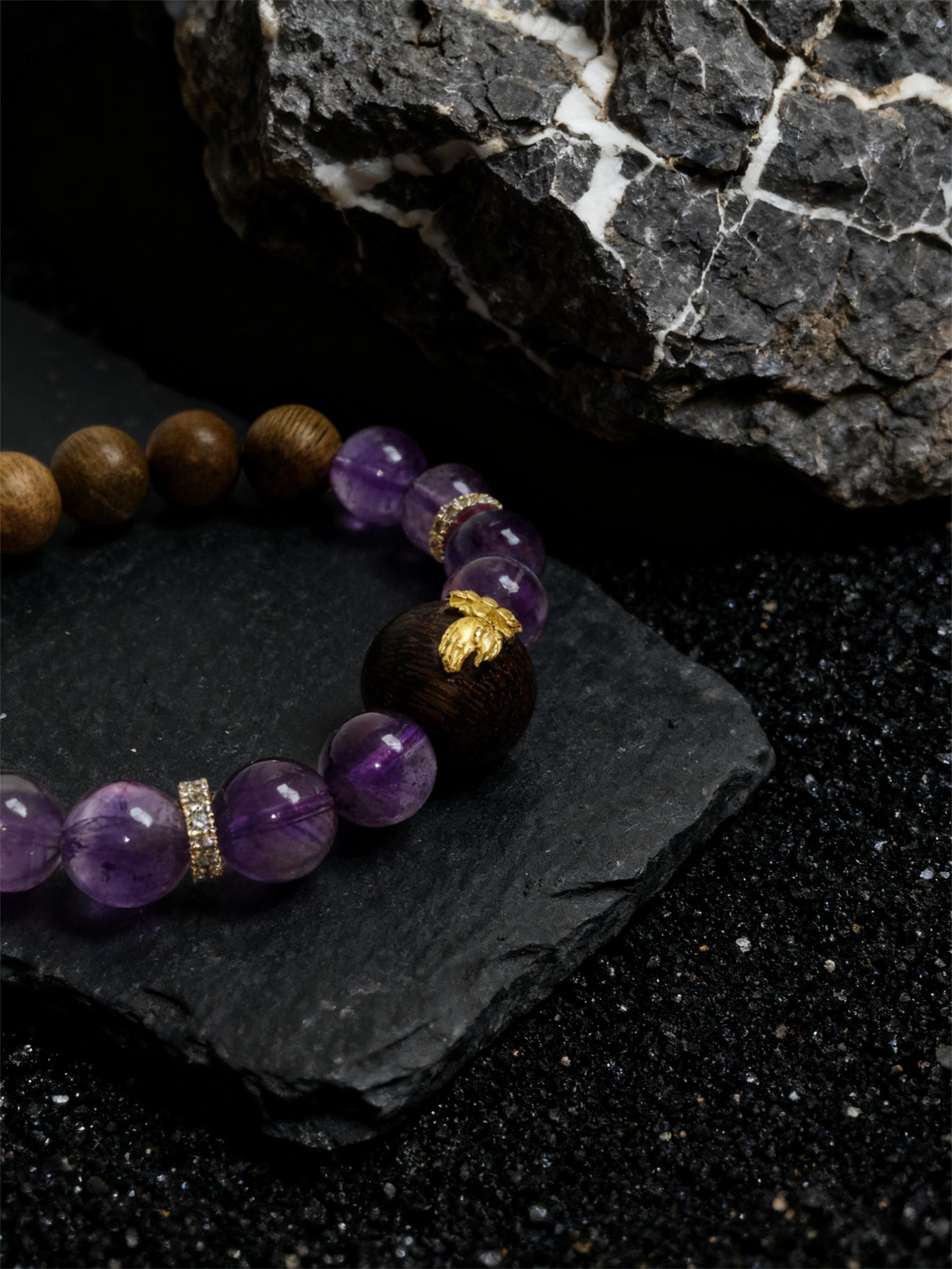 Close-up of the Nüwa inspired Mother of Earth bracelet (11mm) featuring purple beads, a wood accent bead and gold details on a stone background