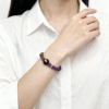 Woman wearing the Nüwa inspired Mother of Earth bracelet (11mm) with purple beads, wood beads and gold details styled with a white shirt