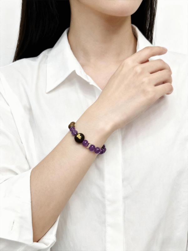 Woman wearing the Nüwa inspired Mother of Earth bracelet (11mm) with purple beads, wood beads and gold details styled with a white shirt