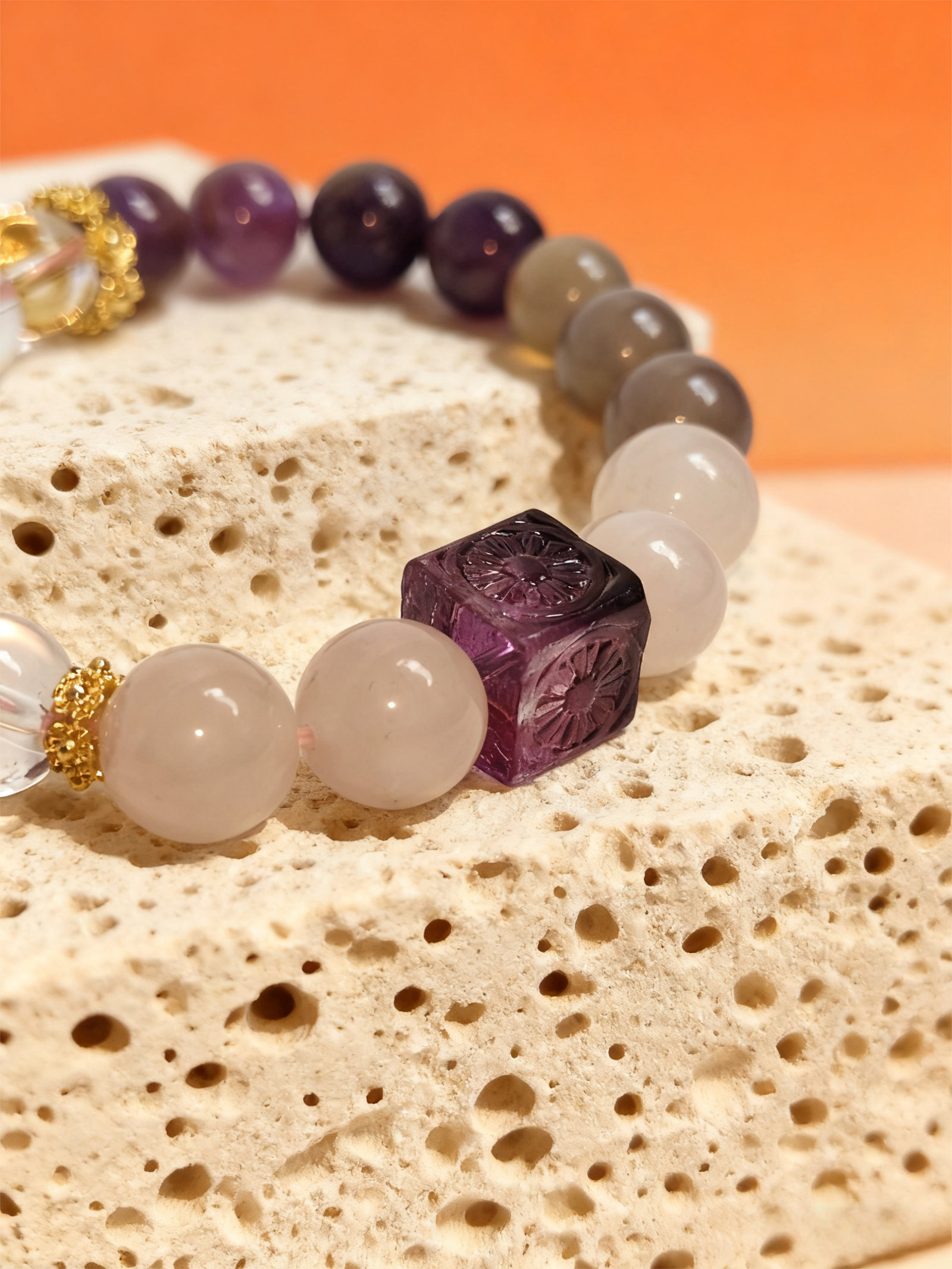Close-up of the Settled Order Bracelet inspired by Nüwa, highlighting the carved purple agate cube and smooth white gemstone beads on a stone surface