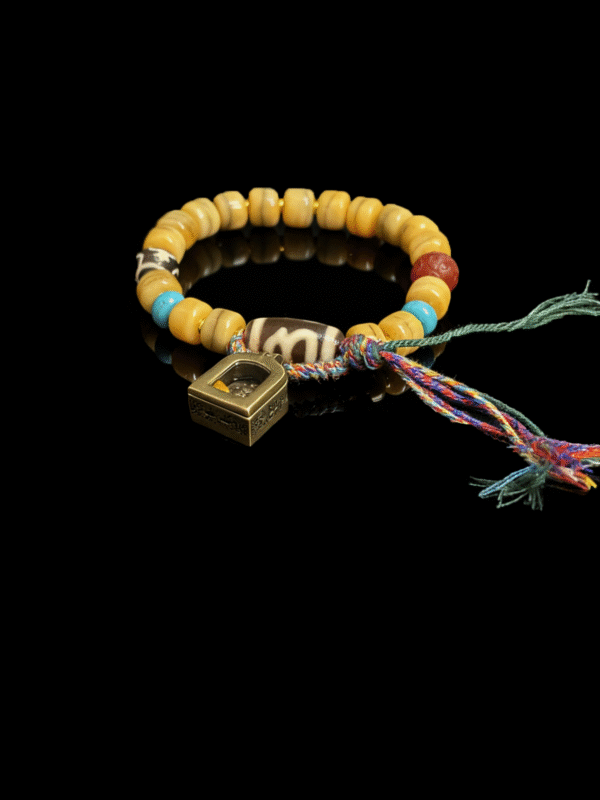 Product view of the Pangu’s Primordial Ethereal Bone-Agate Bracelet (10mm), featuring bone-tone agate beads, a colorful braided tassel cord and a geometric gold charm on a black background