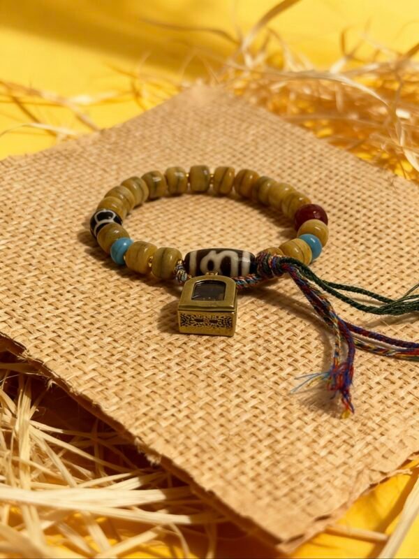 Full view of Pangu inspired bone-agate bracelet with sacred charm box, earthy agate beads and braided cord against warm straw and golden background