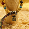 Bone-agate bracelet inspired by Pangu displayed on a woven pillar, featuring symbolic etched bead, yellow agate stones and hanging amulet charm
