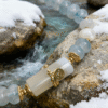 Close-up of the Jingwei inspired Quiet Oath aquamarine bracelet (6mm) with icy blue beads, white accents and gold details photographed by a snowy stream