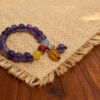 11mm purple translucent beaded bracelet with yellow red blue accent beads and charm on linen and wood background