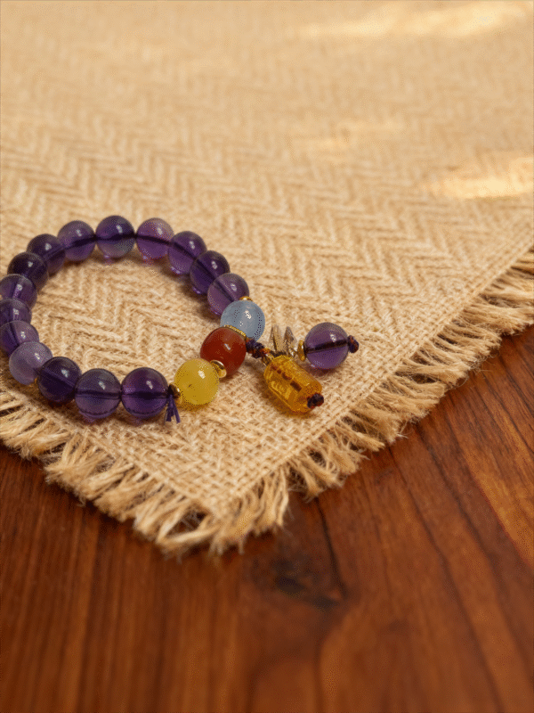 11mm purple translucent beaded bracelet with yellow red blue accent beads and charm on linen and wood background