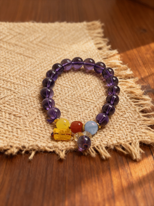 11mm purple translucent beaded bracelet with yellow red blue accent beads and charm on linen and wood background