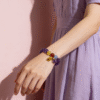 Model wearing the Nüwa inspired Reforged Harmony Bracelet (11mm) with purple translucent beads, colorful accents and charm on a pink background