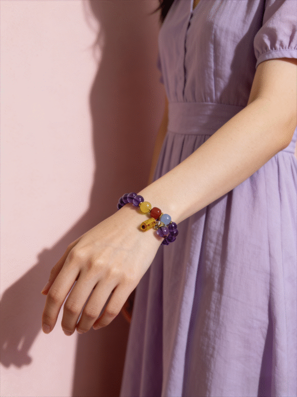 Model wearing the Nüwa inspired Reforged Harmony Bracelet (11mm) with purple translucent beads, colorful accents and charm on a pink background
