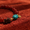 Close-up of the Xingtian inspired Steadfast Heart red agate bracelet (10mm) with turquoise centerpiece, gold details and charm on a red velvet background