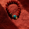 Full view of the Xingtian inspired Steadfast Heart red agate bracelet (10mm) featuring red beads, turquoise center stone and gold charm on a red velvet background