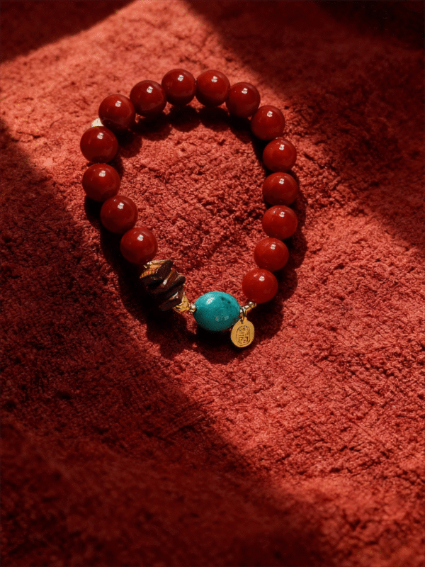 Full view of the Xingtian inspired Steadfast Heart red agate bracelet (10mm) featuring red beads, turquoise center stone and gold charm on a red velvet background
