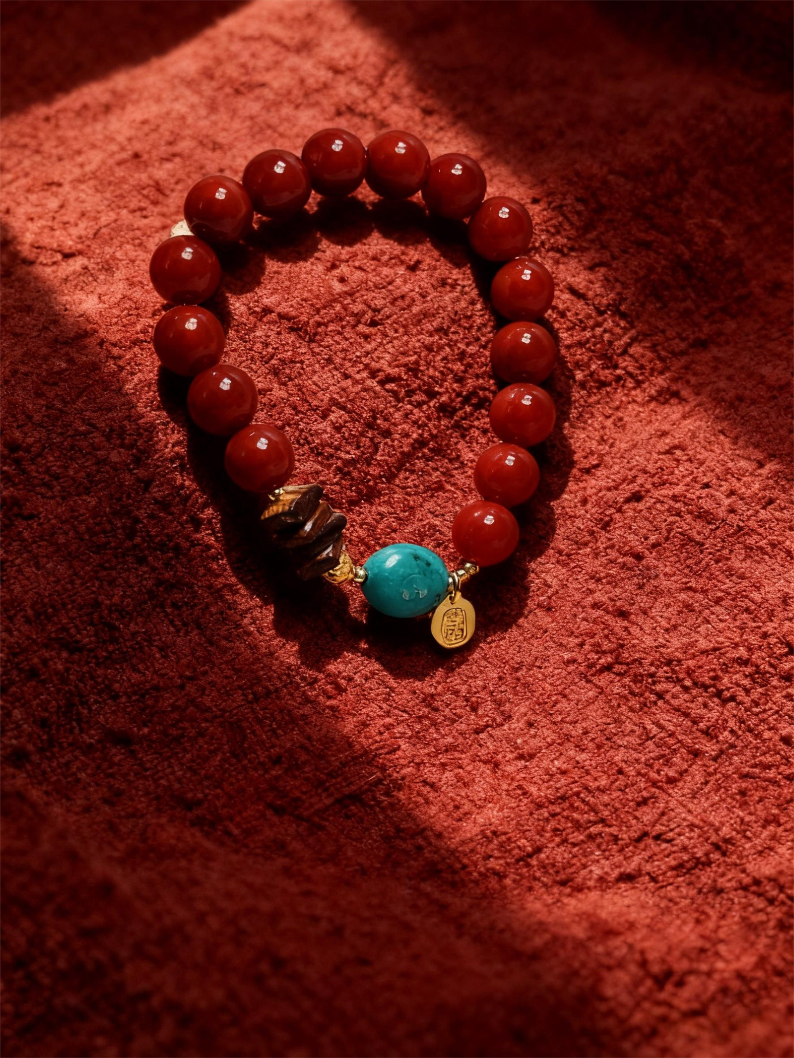 Full view of the Xingtian inspired Steadfast Heart red agate bracelet (10mm) featuring red beads, turquoise center stone and gold charm on a red velvet background