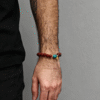 Men’s wrist wearing the Xingtian inspired Steadfast Heart red agate bracelet (10mm) featuring red beads, turquoise centerpiece and gold charm on a grey background