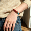 Woman wearing the Xingtian inspired Steadfast Heart red agate bracelet (10mm) with turquoise centerpiece and gold charm in natural light