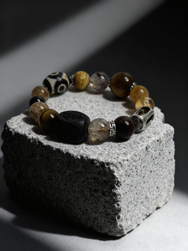 Watchful Relic agate bracelet (12–15mm) with mixed natural stone beads and carved centerpiece, displayed on a textured stone block, luxury handmade myth-inspired jewelry
