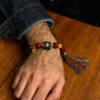 Close-up of Xingtian's Scarlet Agate Bracelet worn on a man's wrist, showcasing red agate beads, symbolic centerpiece and tassel detail