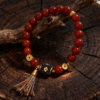 Red agate beaded bracelet inspired by Xingtian, featuring 10mm scarlet agate beads, gold accents, and a symbolic centerpiece displayed on a natural wooden branch