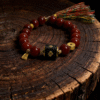 Xingtian’s Scarlet Agate Bracelet with 10mm red agate beads displayed on an ancient wood surface, featuring a central engraved emblem and traditional tassel