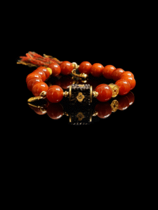 Xingtian’s Scarlet Agate Bracelet featuring polished 10mm red agate beads and a central emblem charm, displayed on a black background with reflective surface.
