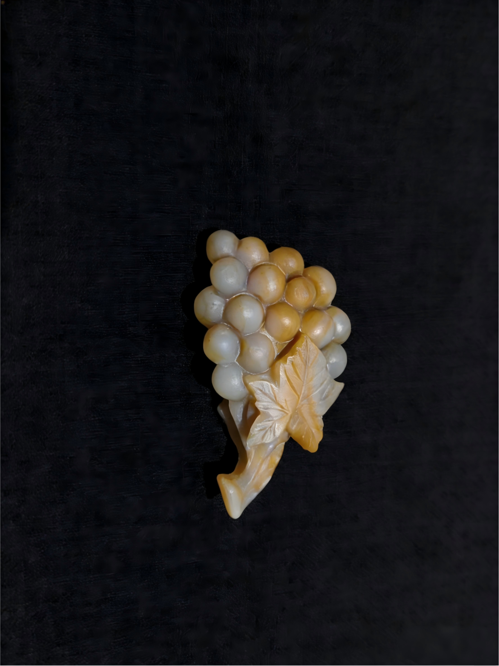 Handheld Agate Artwork titled Blessed Grape, featuring a grape cluster form with rounded bead-like elements and a carved leaf detail in translucent agate