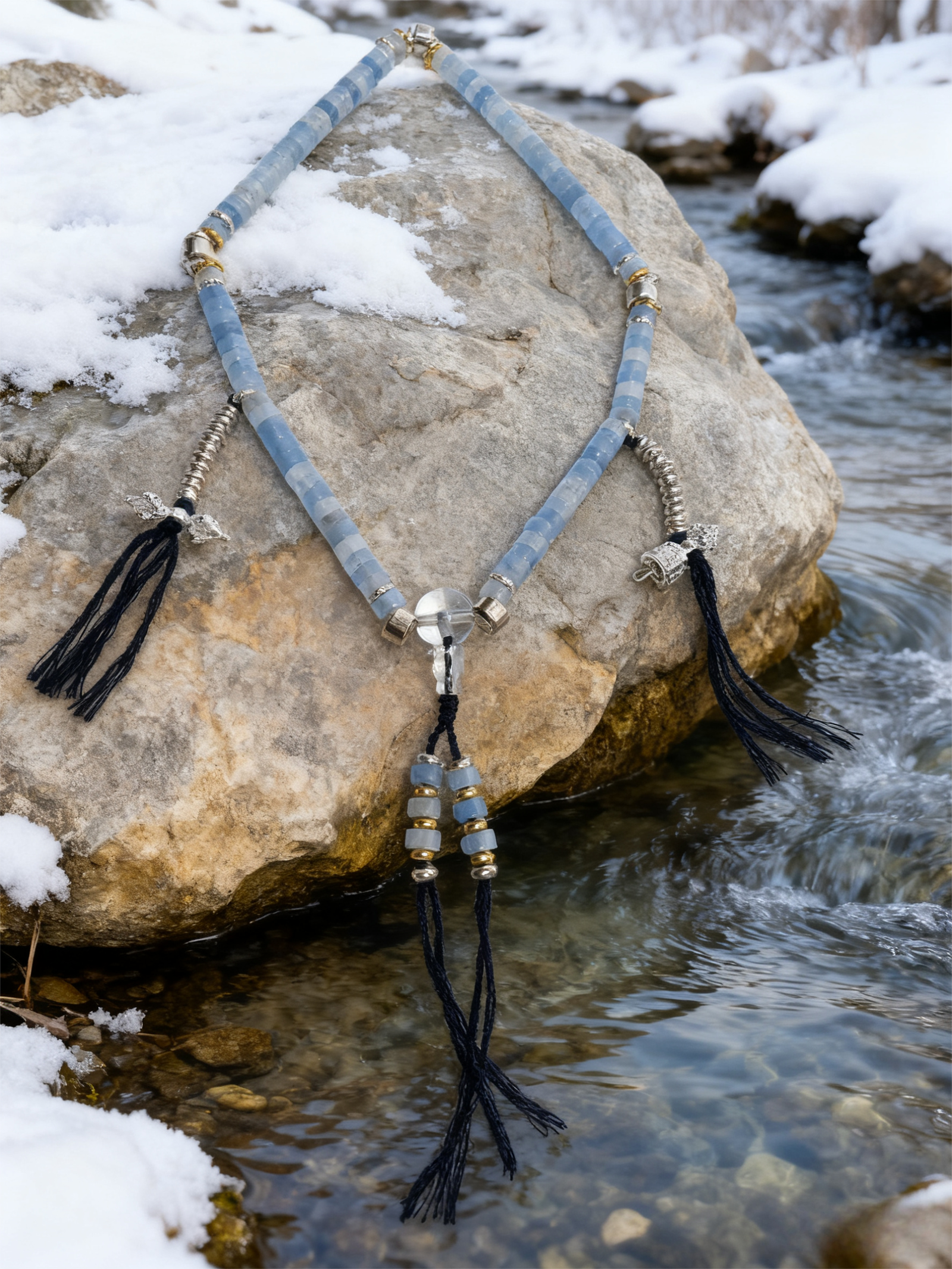 Jingwei-inspired aquamarine and clear quartz bracelet resting on a natural river stone beside flowing water